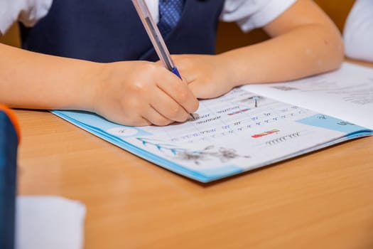 Close-up cropped shot of unrecognizable pupil boy studying at home writing in exercise book doing homework