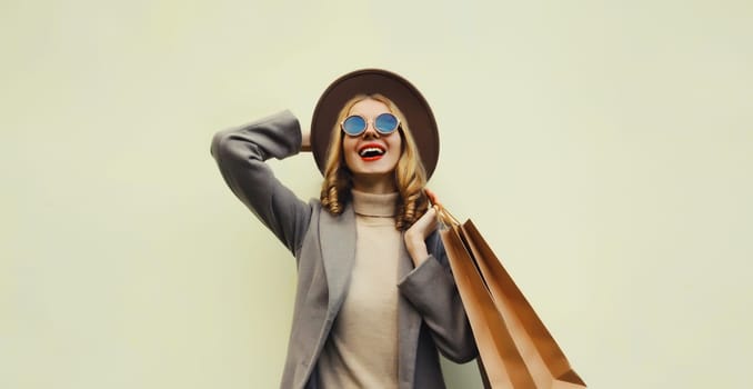 Autumn portrait of happy cheerful young woman with shopping bag, stylish girl in round hat, coat on brown studio background