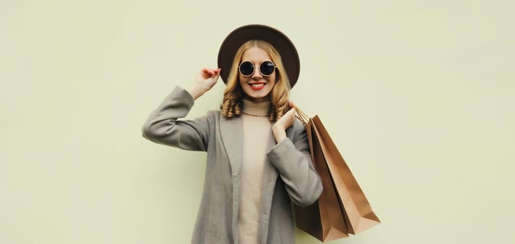 Autumn portrait of beautiful happy young woman with shopping bag, stylish girl in round hat, coat on brown studio background