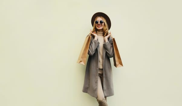Autumn portrait of beautiful happy young woman with shopping bag, stylish girl in round hat, coat on brown studio background