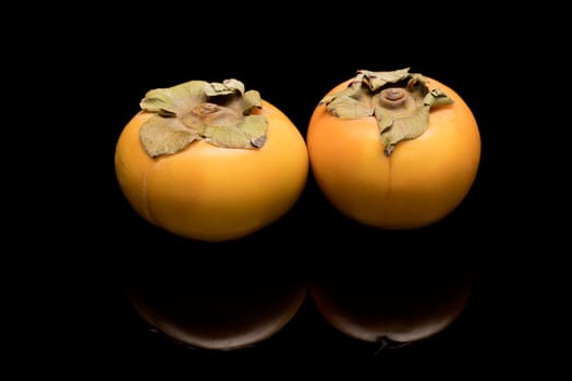 A studio photo of two persimmon fruits on a reflective black surface.
