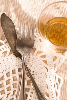 A concept photo of old tarnished fork and butter knife on the table with a mostly empty glass.