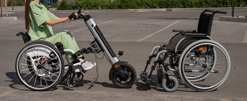 Woman in wheelchair with assistive device for manual control next to classic wheelchair. Electric handbike