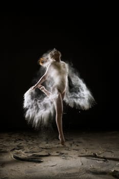 Young slim girl jumping gracefully in white dust cloud artistic studio portrait