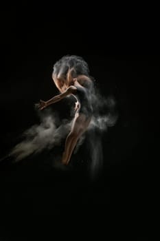Female sexy gymnast in gray bodysuit shot in a jump on black background in a cloud of white dust all over body
