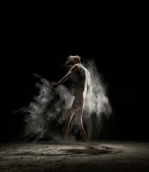 Female sexy gymnast in bodysuit shot in a jump on black background in a cloud of white dust all over body