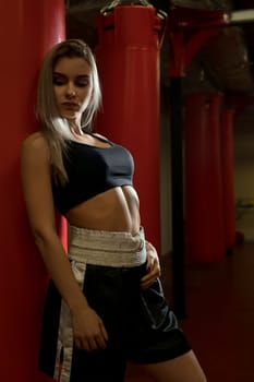 Sexy girl in top and miniskirt posing by punching bag in a gym
