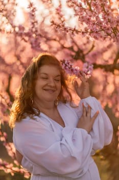 Woman blooming peach orchard. Against the backdrop of a picturesque peach orchard, a woman in a long white dress enjoys a peaceful walk in the park, surrounded by the beauty of nature