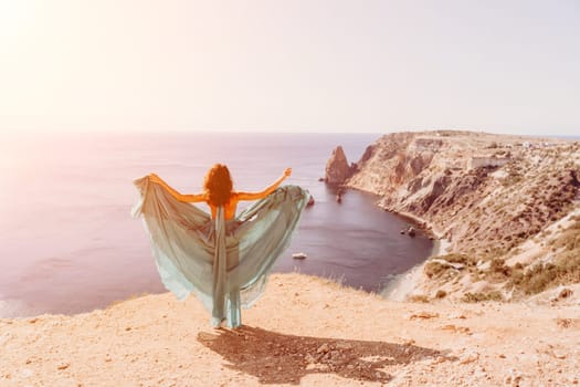 Woman green dress sea. Female dancer posing on a rocky outcrop high above the sea. Girl on the nature on blue sky background. Fashion photo