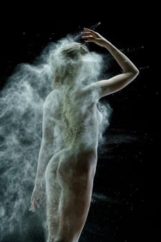 Nude girl posing with her back to viewer in a cloud of white dust in studio