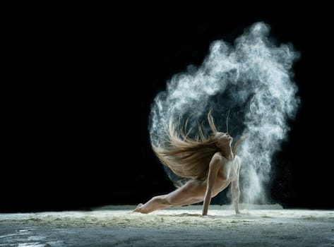 Young girl posing slenderly in a cloud of white dust in studio on black background