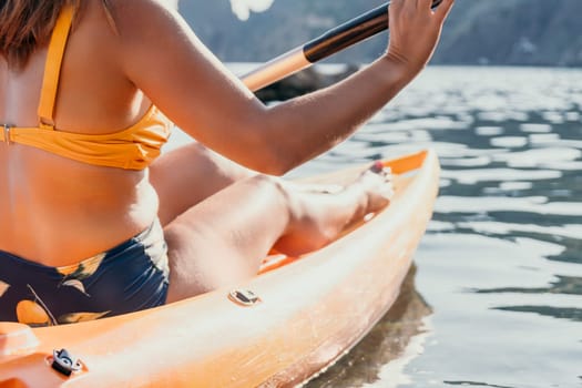 A woman paddles a kayak on calm water. The sun shines on her back as she enjoys the scenery.