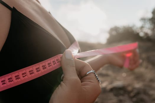 A woman is holding a pink tape measure and is measuring her breasts. The tape measure is marked with numbers, and the woman is looking at it intently