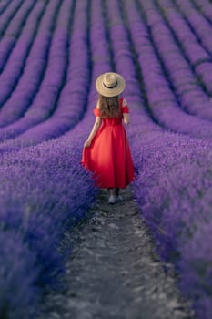 A woman in a red dress is walking through a field of purple flowers. Concept of serenity and beauty, as the woman takes in the natural surroundings