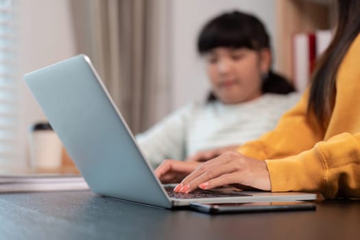 Hands of a focused person typing on a laptop as a young girl observes, representing shared learning and support in a home setting.