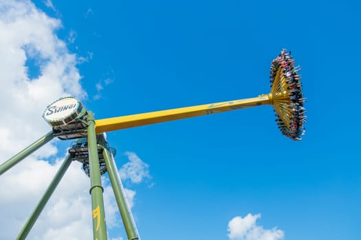 Helsinki, Finland - 19 July 2024: Linnanmaki Amusement Park, new roller coaster Swingi in motion, blue sky on a background, happy people