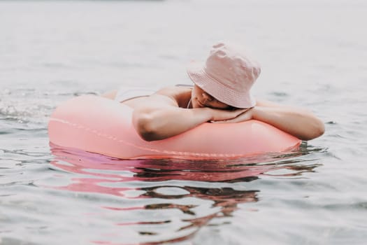 A woman is laying on a pink inflatable raft in the ocean. The scene is peaceful and relaxing, with the woman enjoying the water and the sun