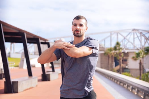 Young sportsman with sports watch stretching before training looking away.