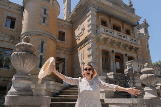 A woman wearing a straw hat is standing in front of a large building. She is smiling and she is happy