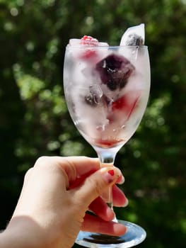 Glass with ice cubes with frozen berries and fruits close-up for a refreshing drink and preservation of seasonal vitamins raspberries, strawberries, cherries, blueberries, mulberries, blackberries
