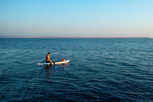 A tourist, sits on a paddleboard or SUP, navigates the tranquil azure sea