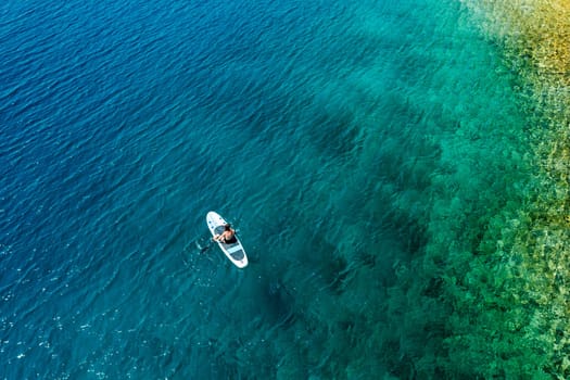A woman glides on a paddleboard near the rocky seaside, navigating the waters with smooth strokes