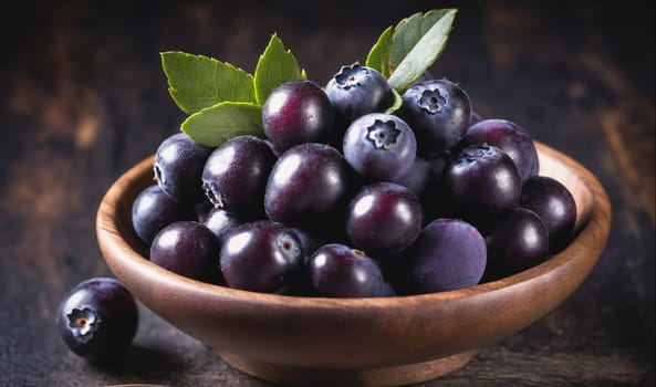A bowl filled with blueberries sits on a wooden table. The blueberries are plump and ripe, and there are a few green leaves scattered throughout the bowl. The bowl is made of dark wood and has a natural finish. The table is also made of wood, and the background is a blurred image of a dark, rustic wall.