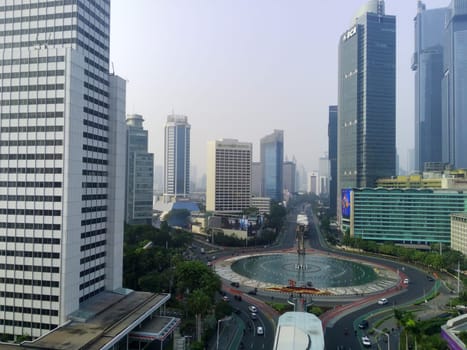 Aerial view of Bundaran HI, a bustling roundabout in Jakarta, Indonesia. Skyscrapers, traffic, and the Selamat Datang monument create a dynamic cityscape.