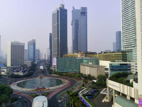 Aerial view of Bundaran HI, a bustling roundabout in Jakarta, Indonesia. Skyscrapers, traffic, and the Selamat Datang monument create a dynamic cityscape.