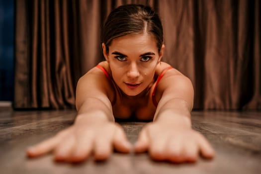 Young woman in red corset and black leather pants. Sexy seductive brunette, fitness instructor doing stretching and pilates on yoga mat at home. Female fitness yoga concept. Role play. Entertainment