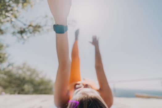 A woman in an orange sports bra performs yoga outdoors, her arms extended towards the sky.