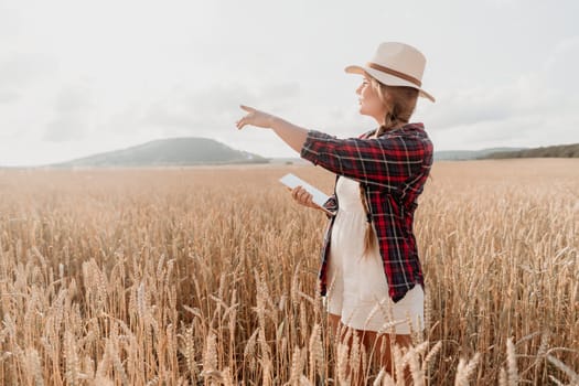 A young woman wearing a white hat and plaid shirt stands in a wheat field, pointing towards the horizon, holding a tablet.