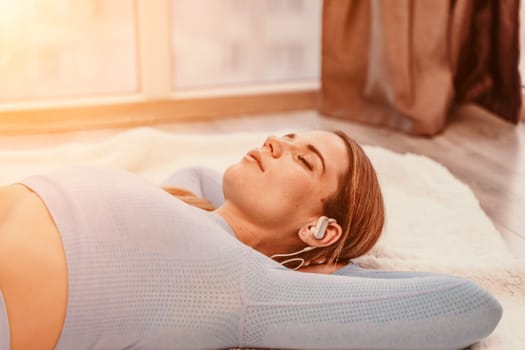 Side view portrait of relaxed woman listening to music with headphones lying on carpet at home. She is dressed in a blue tracksuit