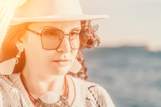 Portrait of a curly haired woman in a white hat and glasses on the background of the sea