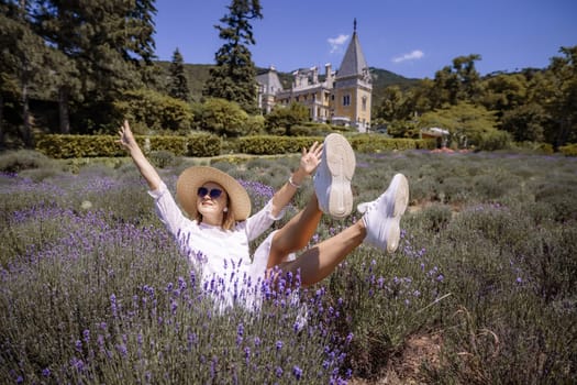 A woman is laying in a field of purple flowers, wearing a white dress and a straw hat
