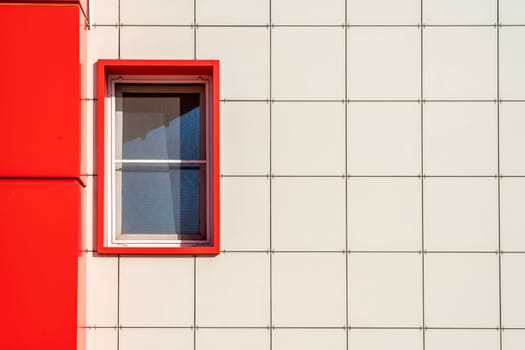 A bright red window frame stands out against the sleek white facade of a contemporary building. Natural light highlights the simplicity of the design, showcasing urban architecture.