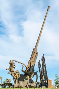 An artillery piece stands prominently in a park, showcasing its imposing structure against a backdrop of fluffy clouds. This piece represents historical military technology from the past.