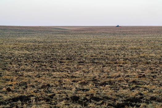 A tractor works diligently on expansive farmland, tilling the soil as the early morning light casts a soft glow. The landscape stretches endlessly, showcasing the open fields.