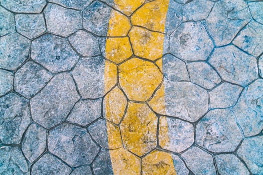 The surface features a unique arrangement of hexagonal stones, with a distinct yellow line curving across the pavement, highlighting the texture and color contrast in a public space.
