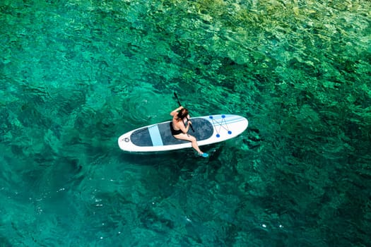 Woman paddling near the rocky seaside using paddle board or SUP.