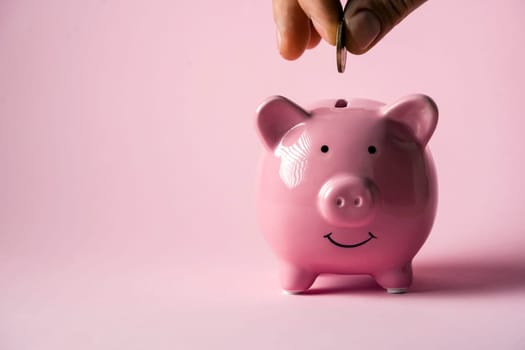 The hand holds a coin and puts it in a piggy bank to preserve wealth, savings and financial success.