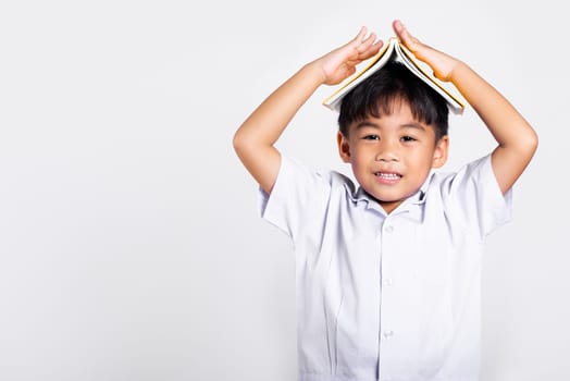 Asian adorable toddler smiling happy wearing student thai uniform red pants stand holding book over head like roof in studio shot isolated on white background, Portrait little children boy preschool