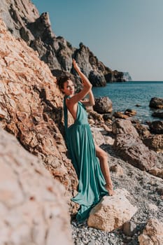 Woman green dress sea. Woman in a long mint dress posing on a beach with rocks on sunny day. Girl on the nature on blue sky background