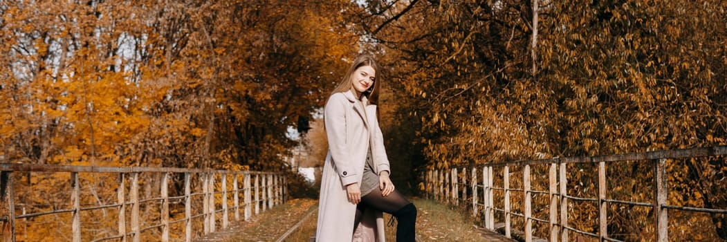 A beautiful long-haired woman walks through the autumn streets. Railway, autumn leaves, a woman in a light coat.