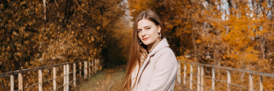 A beautiful long-haired woman walks through the autumn streets. Railway, autumn leaves, a woman in a light coat.