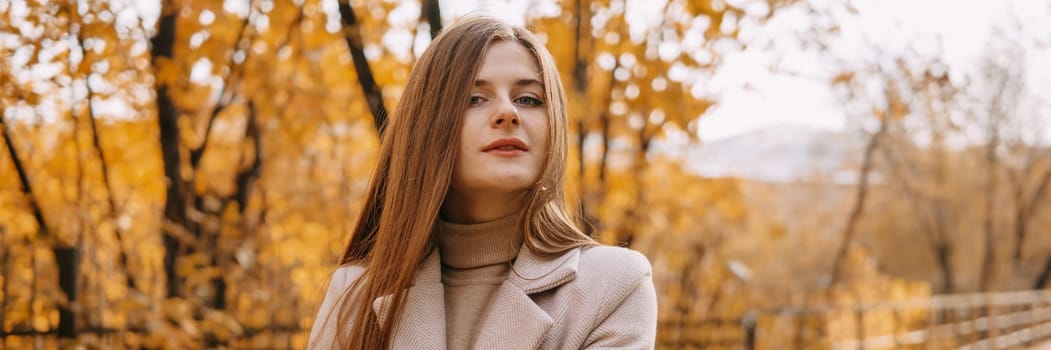 A beautiful long-haired woman walks through the autumn streets. Railway, autumn leaves, a woman in a light coat.