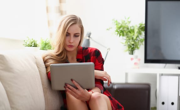 pretty blond young woman surfing the internet hold laptop in arms search information sit on sofa