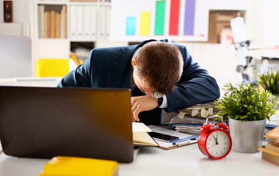 Red alarm clock shows late time closeup and tired office male clerk in suit take nap on table workplace full of exam papers. Career frustration freelance employment fail study problem low energy down