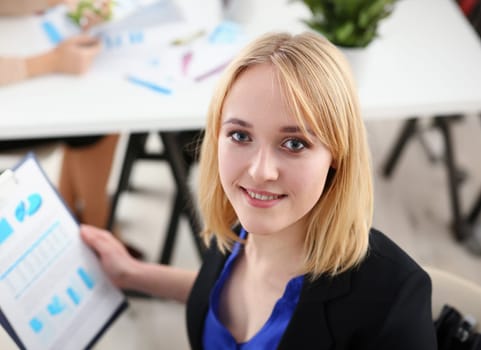 Beautiful smiling cheerful girl at workplace look in camera with colleagues group in background. White collar worker at workspace job offer modern lifestyle client visit profession train concept