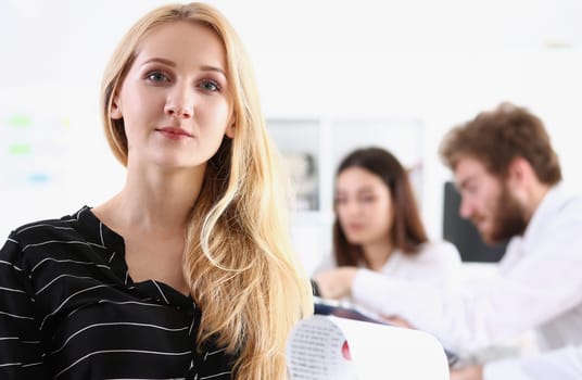 Beautiful smiling cheerful girl at workplace look in camera with colleagues group in background. White collar worker at workspace job offer modern lifestyle client visit profession train concept